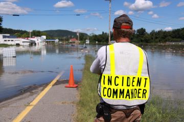 Fire chief with his back to the camera looking over flooded streets in Westminster, Vermont